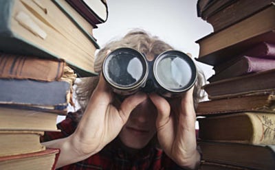 Personne regardant à travers des jumelles entre deux piles de livres