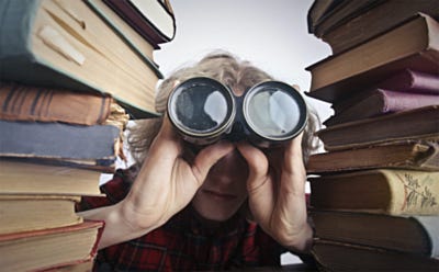 Personne regardant à travers des jumelles entre deux piles de livres