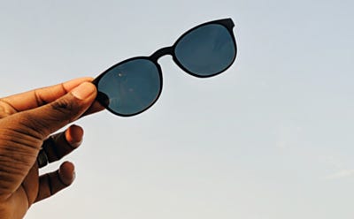 Paire de lunettes de soleil tenue à la main sur fond de ciel dégagé