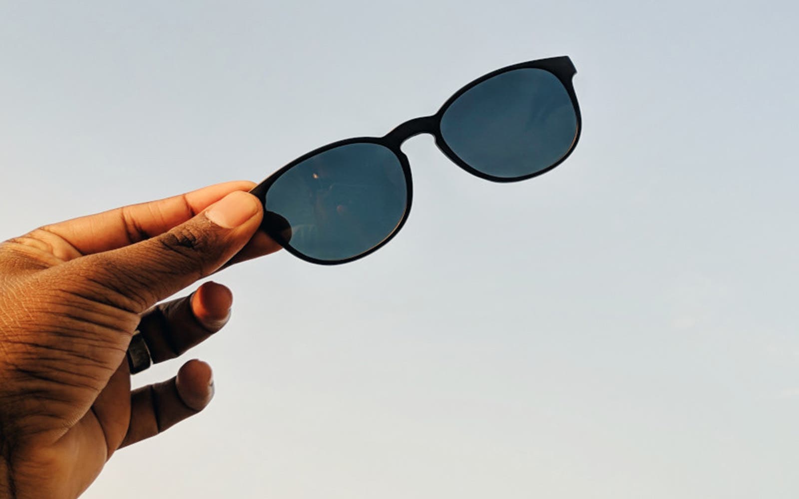 Paire de lunettes de soleil tenue à la main sur fond de ciel dégagé